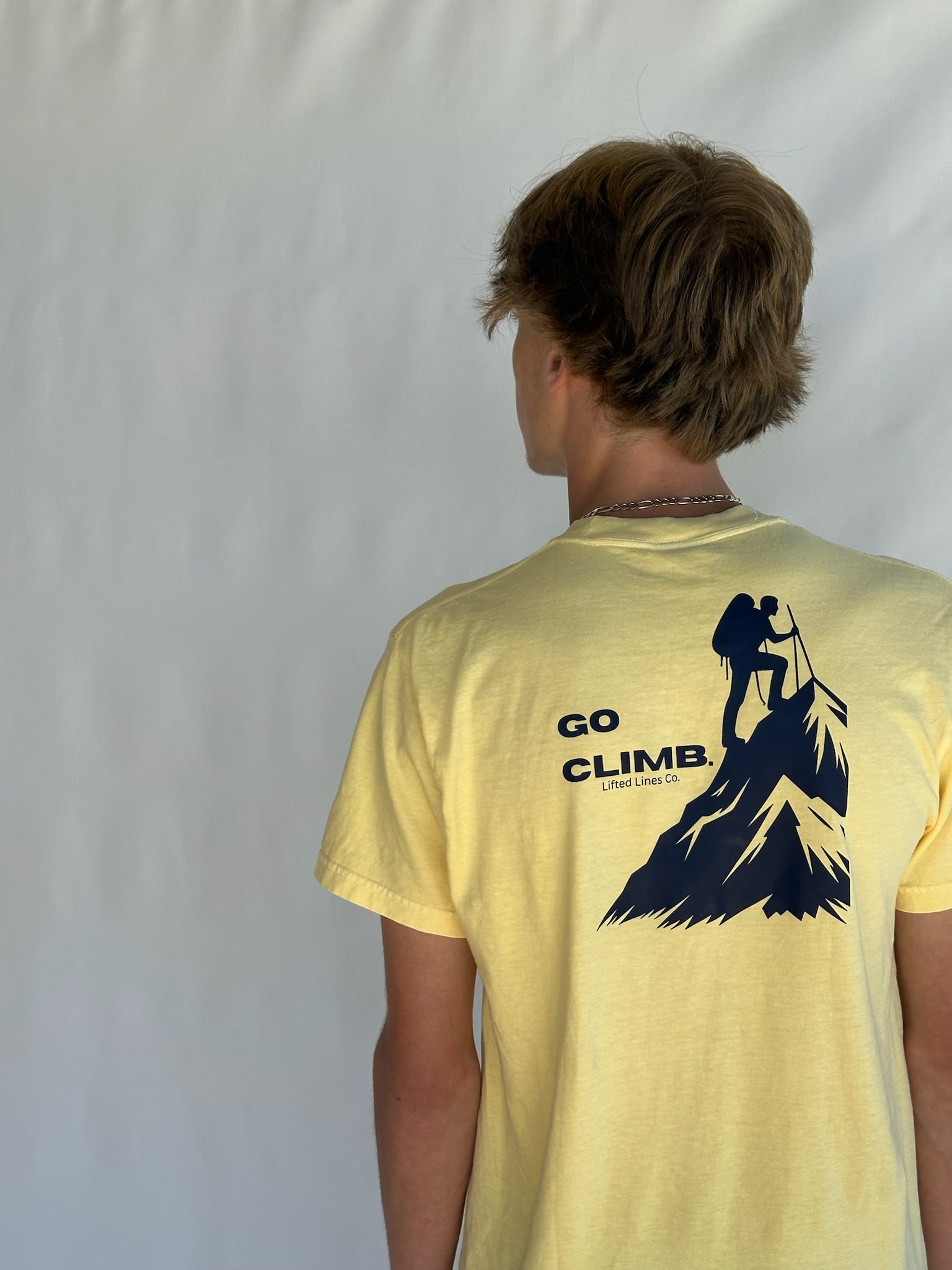 Person wearing a yellow t-shirt with 'GO CLIMB' and mountain graphic on the back against a white background
