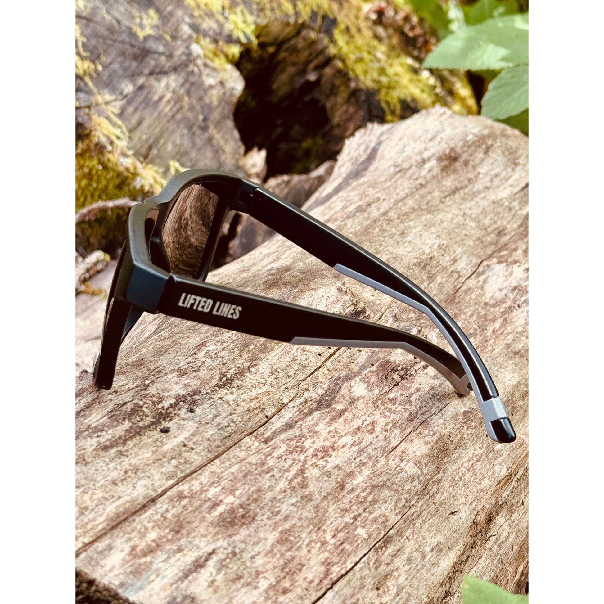Black sunglasses with 'Lifted Lines' branding on a wooden surface with natural background