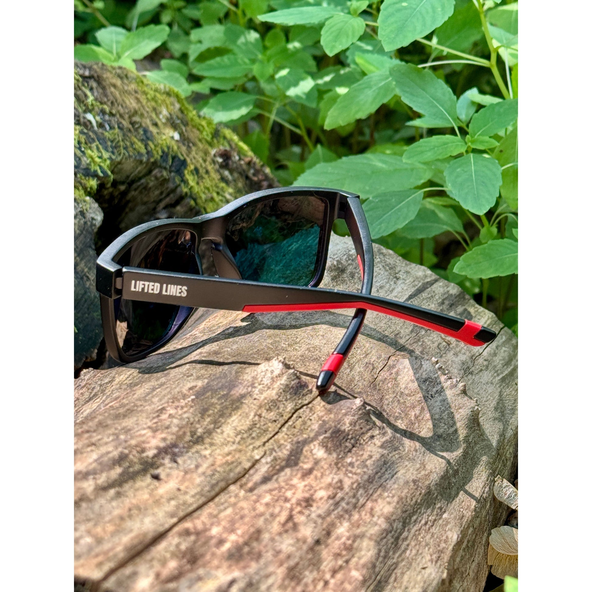 Sunglasses with red accents on a wooden surface with green foliage in the background